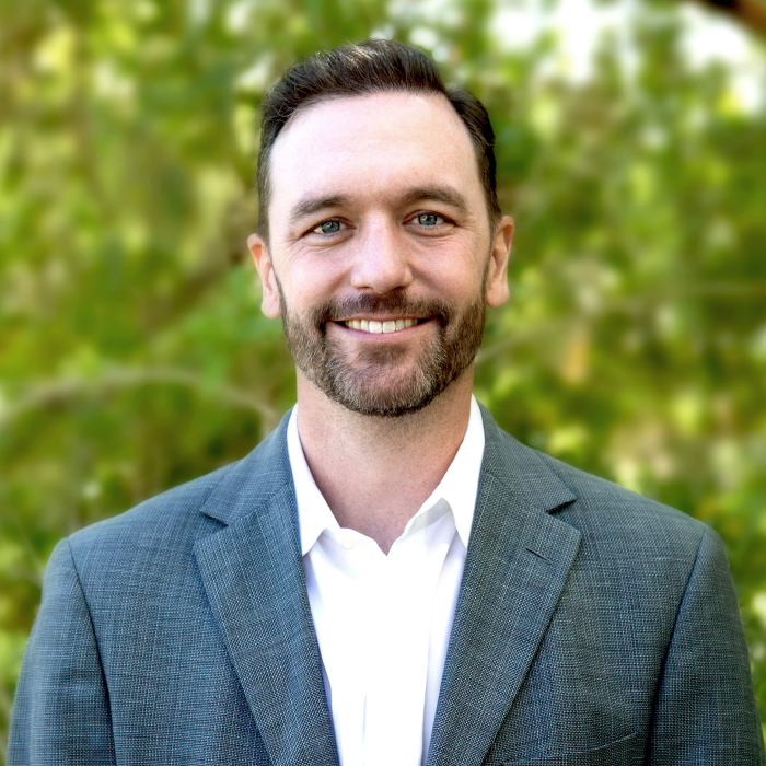 A headshot of Chris Fox with green foliage in the background.