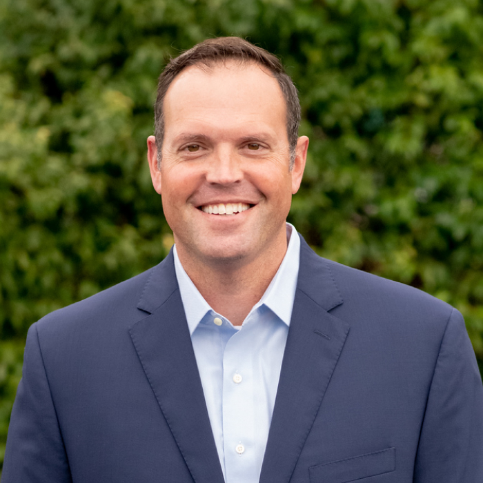 A headshot of Dan Summa with green foliage in the background.