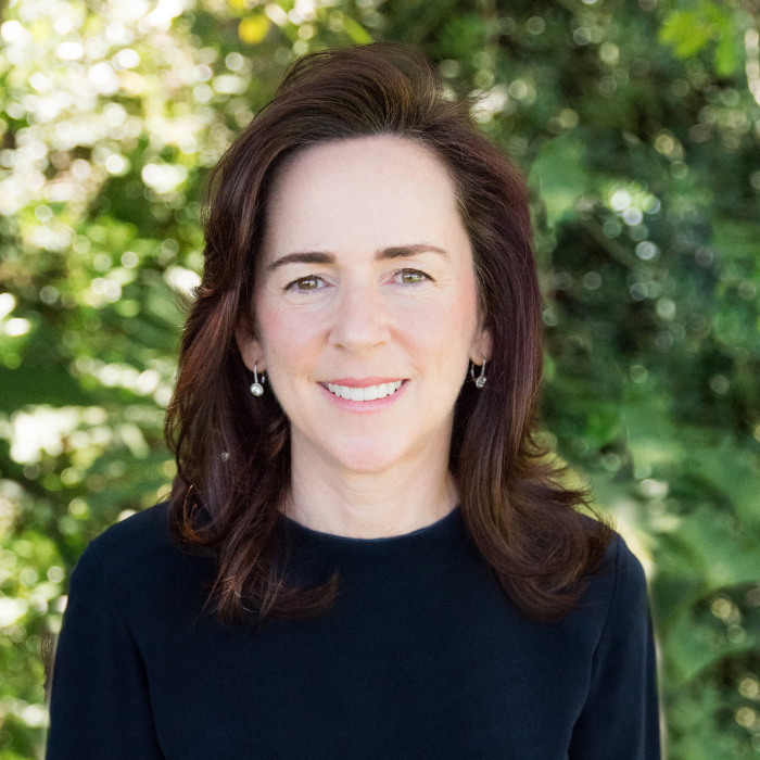 A headshot of Jennifer Hein with green foliage in the background.