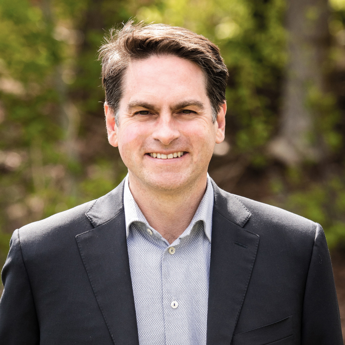 A headshot of Steve Ryder with green foliage in the background.