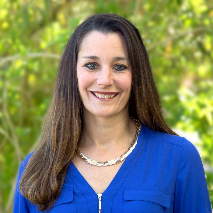 A headshot of Susan Barlow with green foliage in the background.