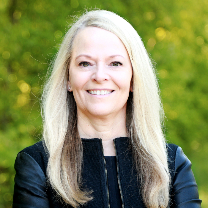 A headshot of Valerie Wooley with green foliage in the background.