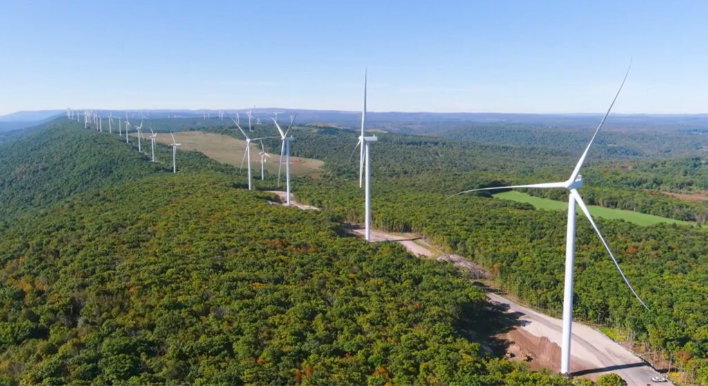 Wind turbines from aerial view with blue skies and luscious green grass.